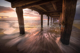Seaford Pier in Melbourne Australia during sunset on a summer evening. The sun light is reflection of the pier and sand to create exceptionally vibrant colours.