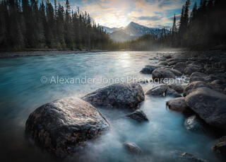 sunrise over snow capped mountains onto athabasca river rocks in banff national park in canadian rocky mountains