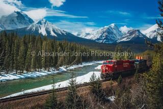 train going through morants curve in banff national park in canadian rocky mountains in spring with snow capped mountains in the distance 