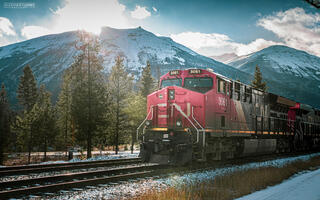 sun shining on freight train with snow capped mountains in the distance in the canadian rocky mountains in Jasper National Park