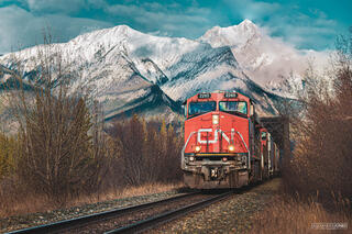 CN train going over bridge past snow capped mountains in canadian rocky mountains
