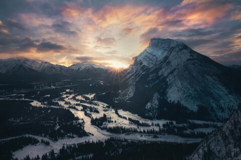 sun bursting over horizon next to rundle mountain in banff national park