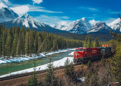 train going through morants curve in banff national park in canadian rocky mountains in spring with snow capped mountains in the distance 