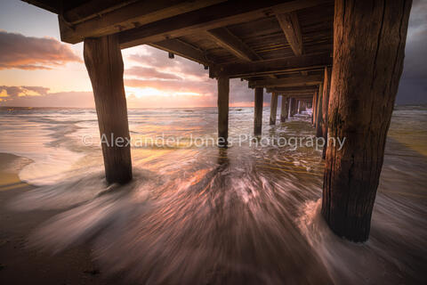 Seaford Pier in Melbourne Australia during sunset on a summer evening. The sun light is reflection of the pier and sand to create exceptionally vibrant colours.