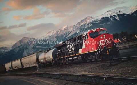 a CN train in during sunset with snow capped mountains in the background