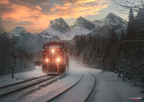 freight train in winter and snow going past mountains during sunrise