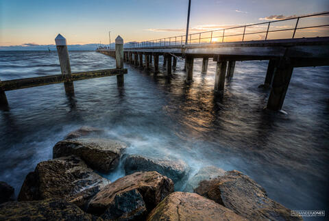 Sun setting over a pier in melbourne australia with light bouncing off rocks