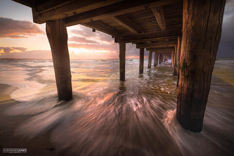 Seaford Pier in Melbourne Australia during sunset on a summer evening. The sun light is reflection of the pier and sand to create exceptionally vibrant colours.