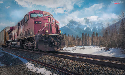 Freight train going past three sisters mountains in Canmore Alberta on a sunny afternoon in winter or spring. 