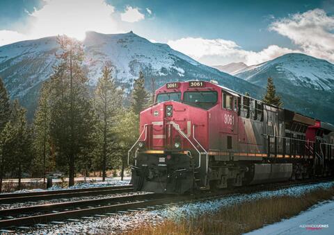 sun shining on freight train with snow capped mountains in the distance in the canadian rocky mountains in Jasper National Park