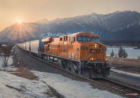 train during sunset with snow-capped mountains in the distance in the Canadian rocky mountains 