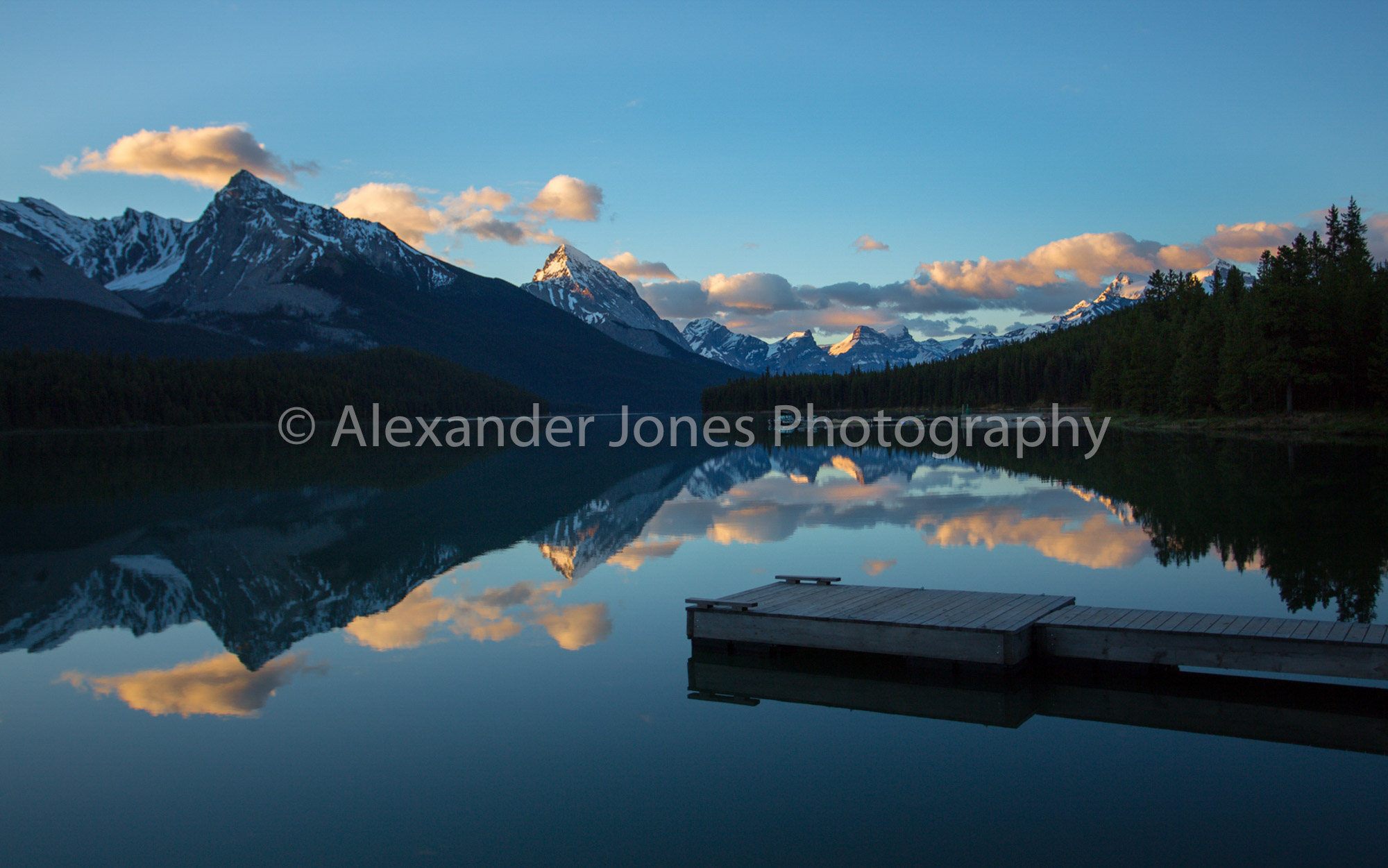 Mirror reflection during sunrise over Maligne Lake and pier in Jasper National Park in Canadian Rocky Mountains