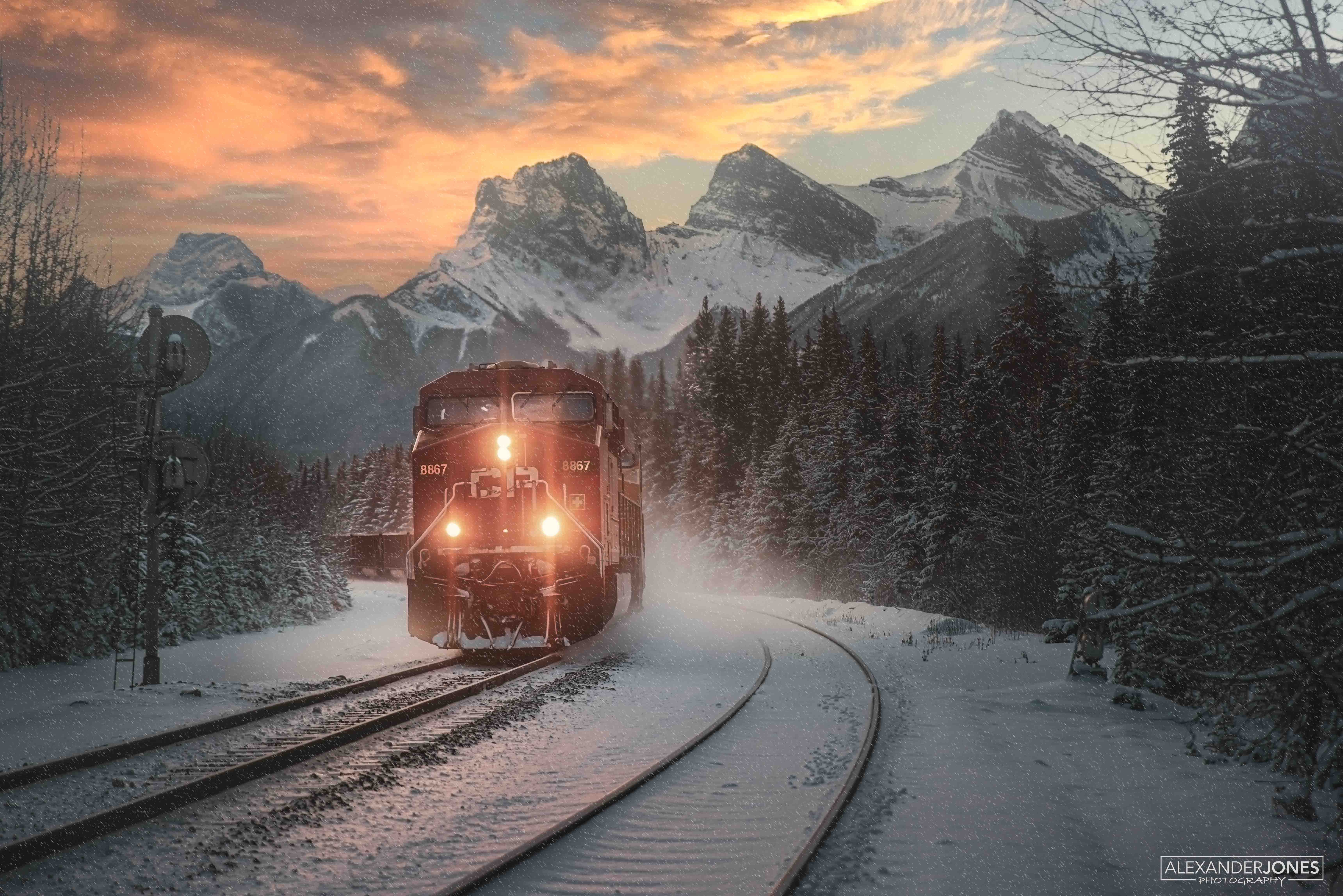 freight train in winter and snow going past mountains during sunrise